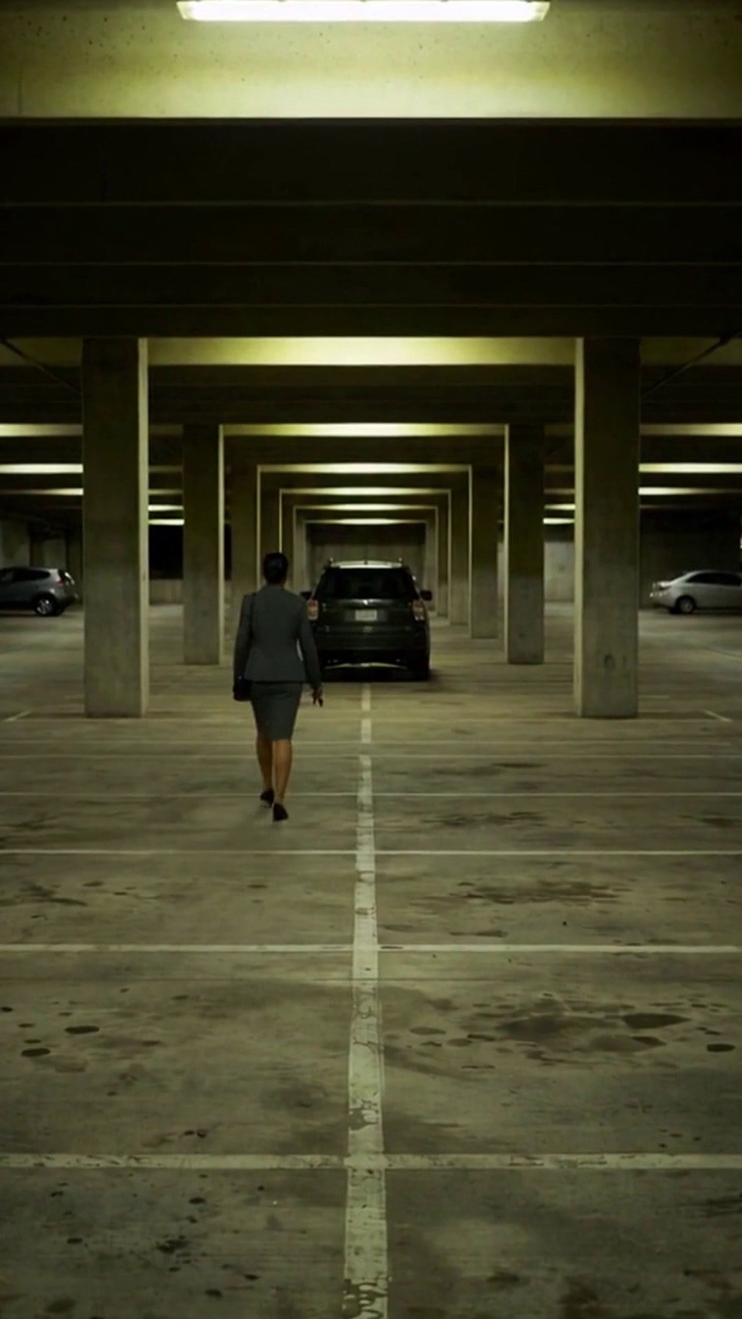 A woman in a business suit walking alone across an empty parking garage level toward her SUV - Ankin Law dramatization