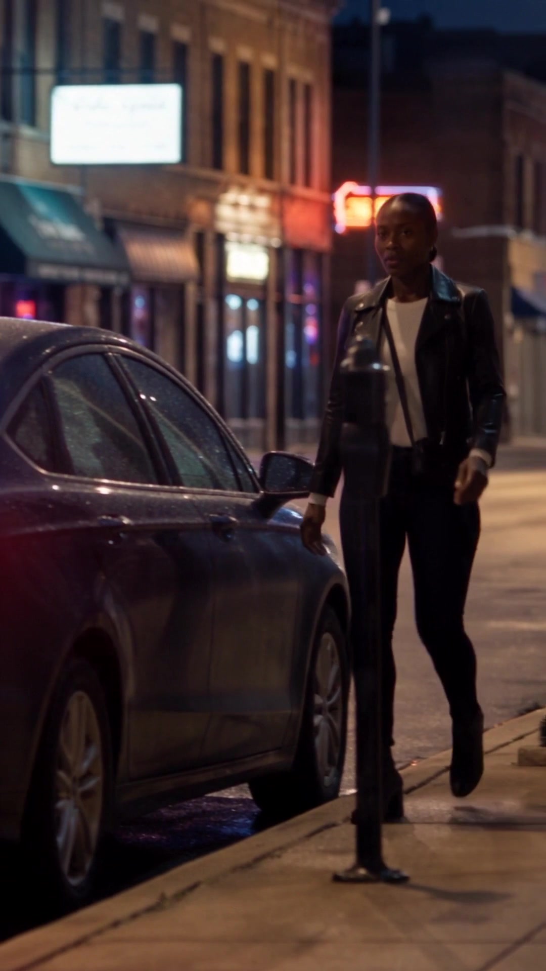 A woman in a leather jacket getting into the back of a car on a busy city street at night - Ankin Law dramatization