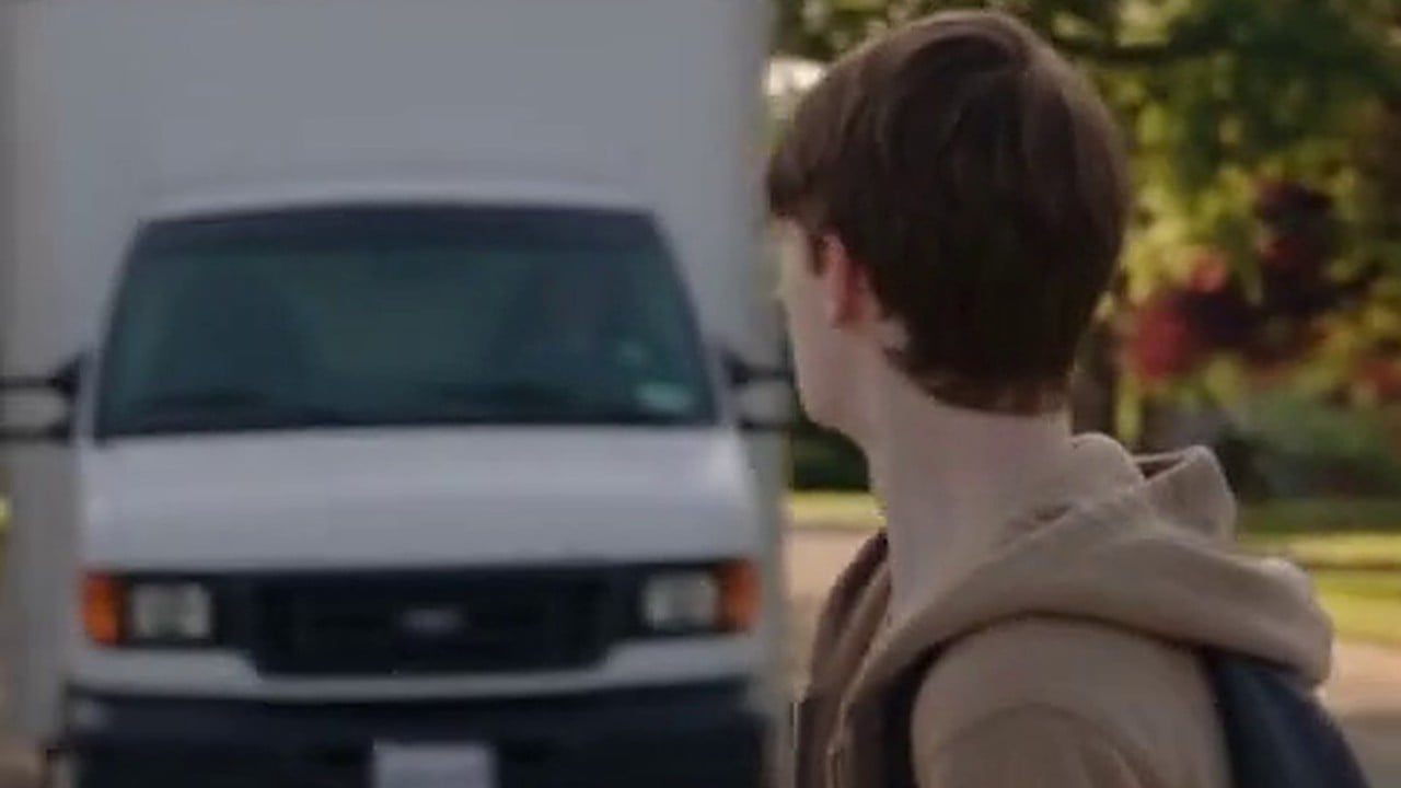 A teenager in a marked crosswalk as a box truck runs the light toward him
