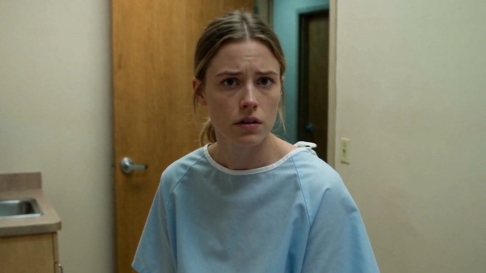 A frightened young woman in a hospital gown on an exam table