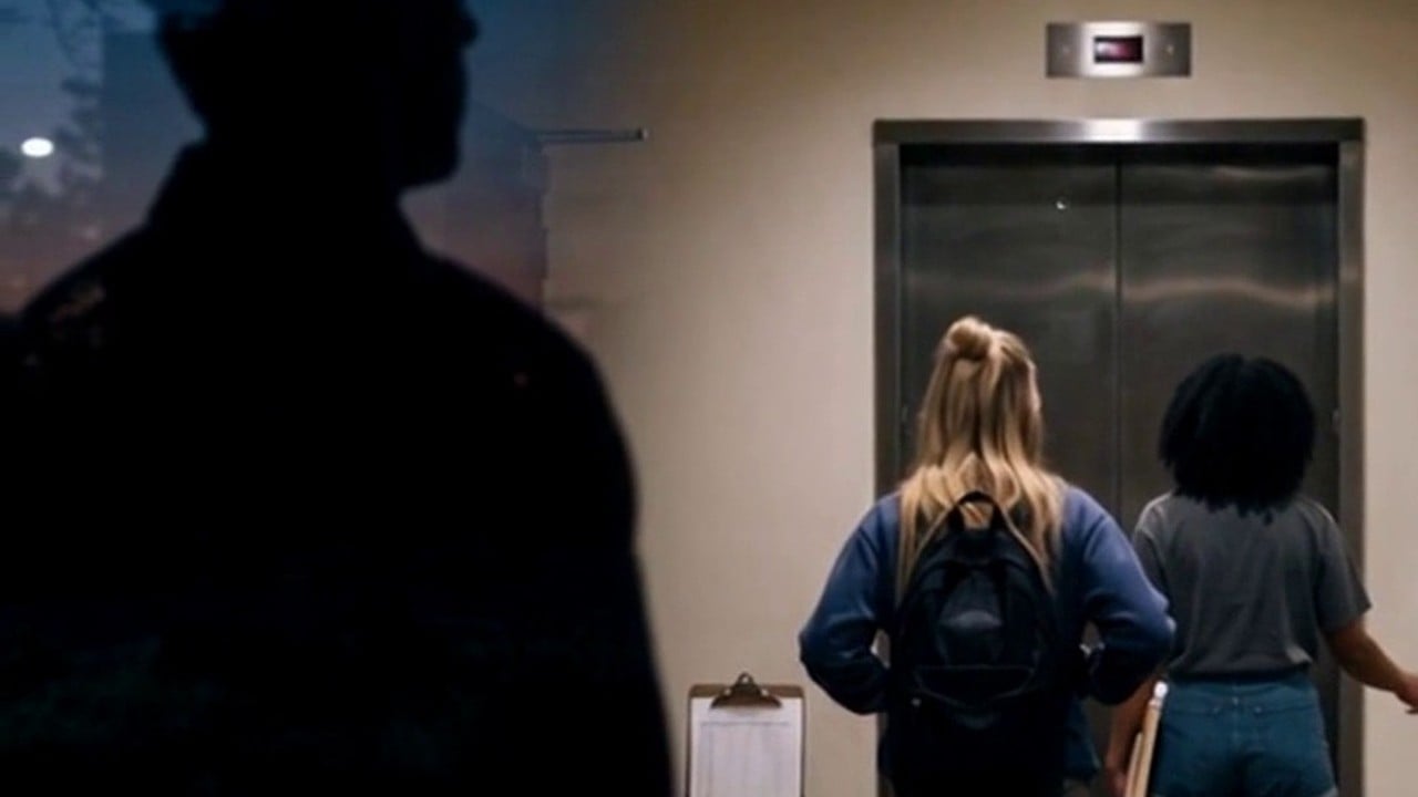 A stranger watching two college students through the glass door of a residence hall with an empty front desk