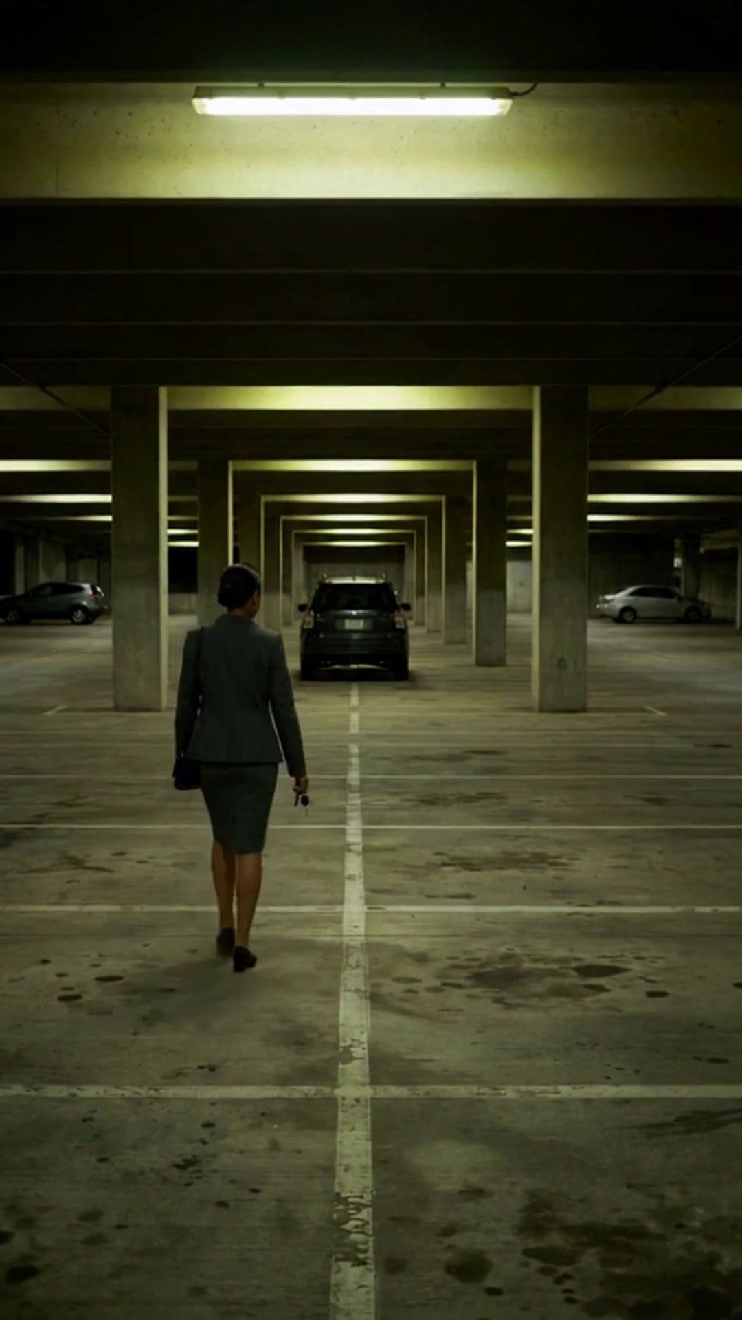 A woman walking across the painted lanes of a parking garage level toward her vehicle - Ankin Law dramatization