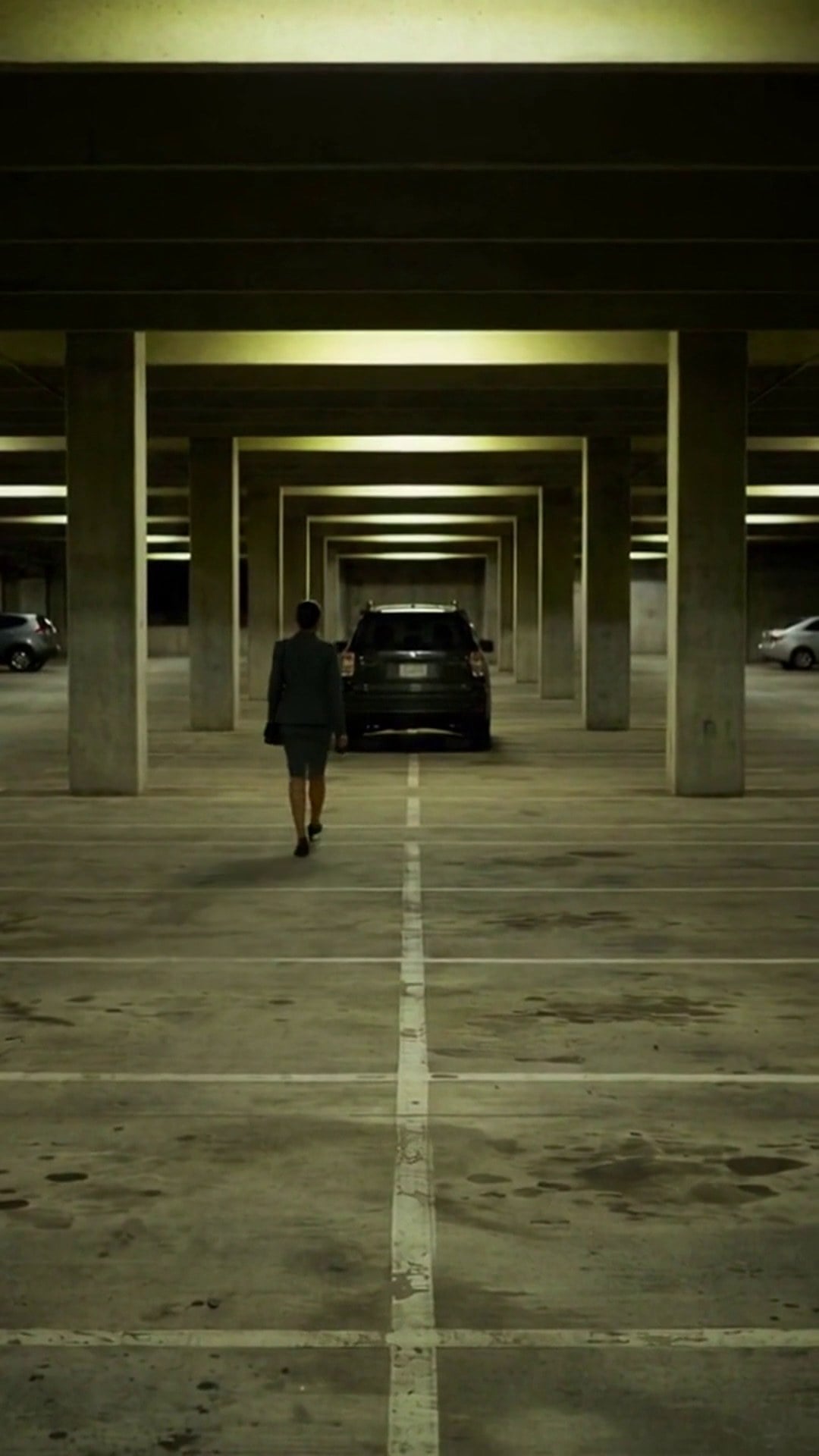 A lone woman far down an empty concrete parking garage between rows of pillars - Ankin Law dramatization