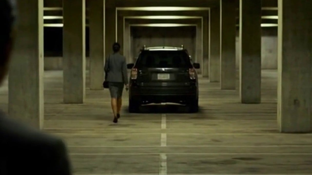A figure stepping out from behind a pillar as a woman reaches her car in an empty parking garage