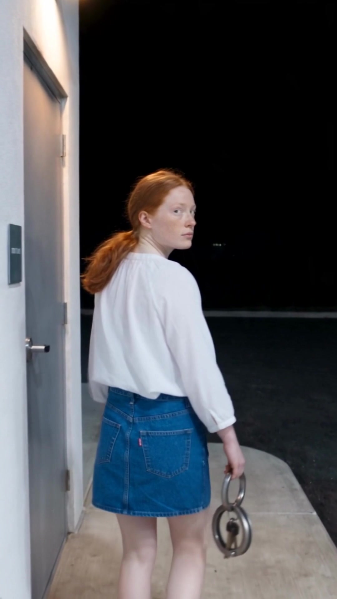 A young woman glancing back over her shoulder at a dark gas station forecourt as she reaches the restroom door - Ankin Law dramatization