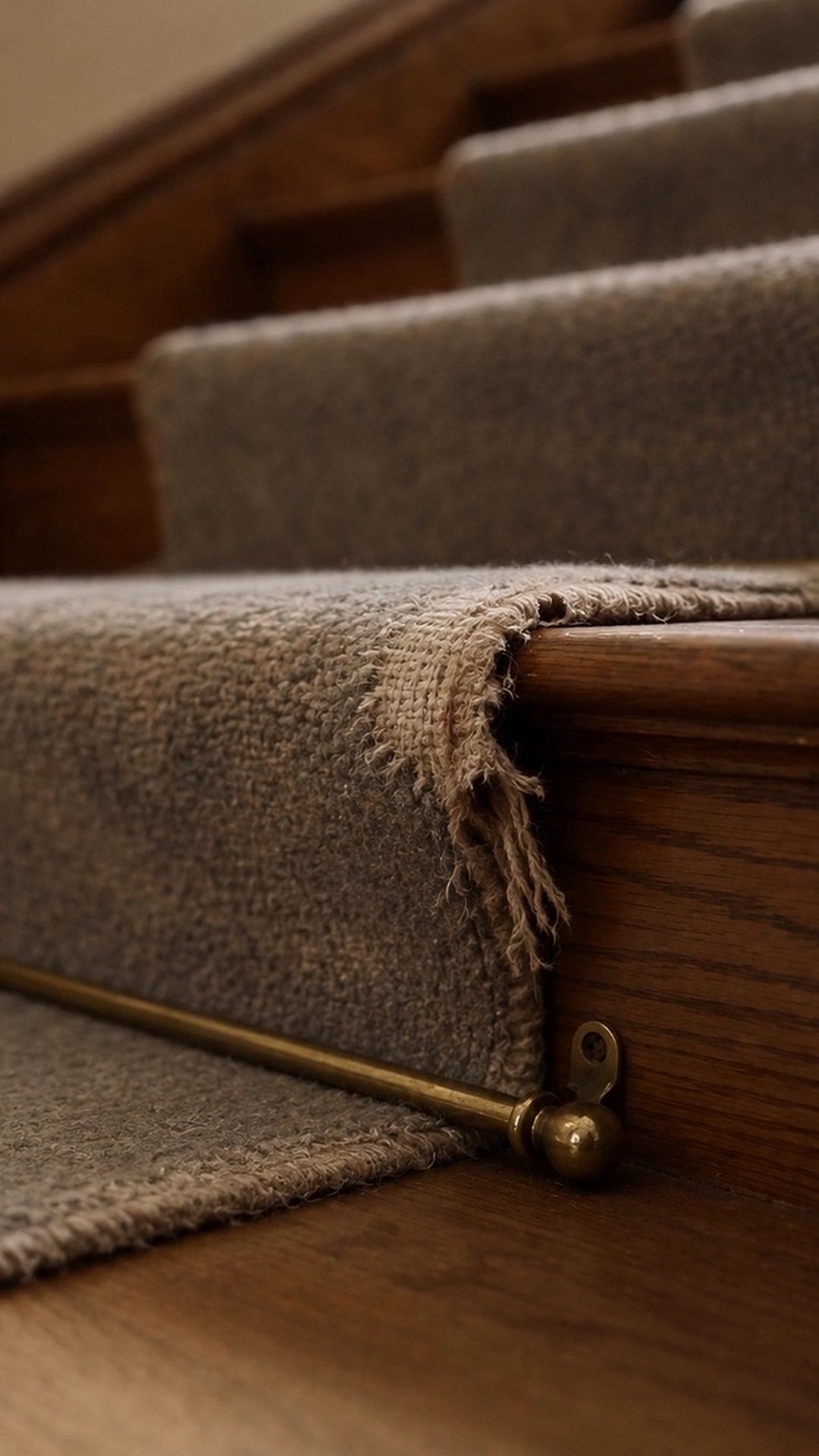 The frayed, worn-through front edge of a carpet stair runner above a brass stair rod - Ankin Law dramatization